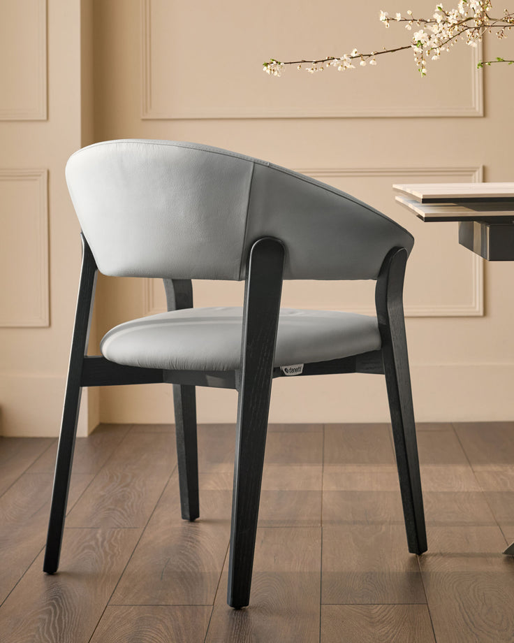 Amelia dining chair in light grey leather with black wooden frame, shown in room setting with beige walls.