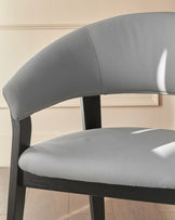 Amelia dining chair in light grey leather with dark wood frame, shown from a side angle highlighting the curved backrest.