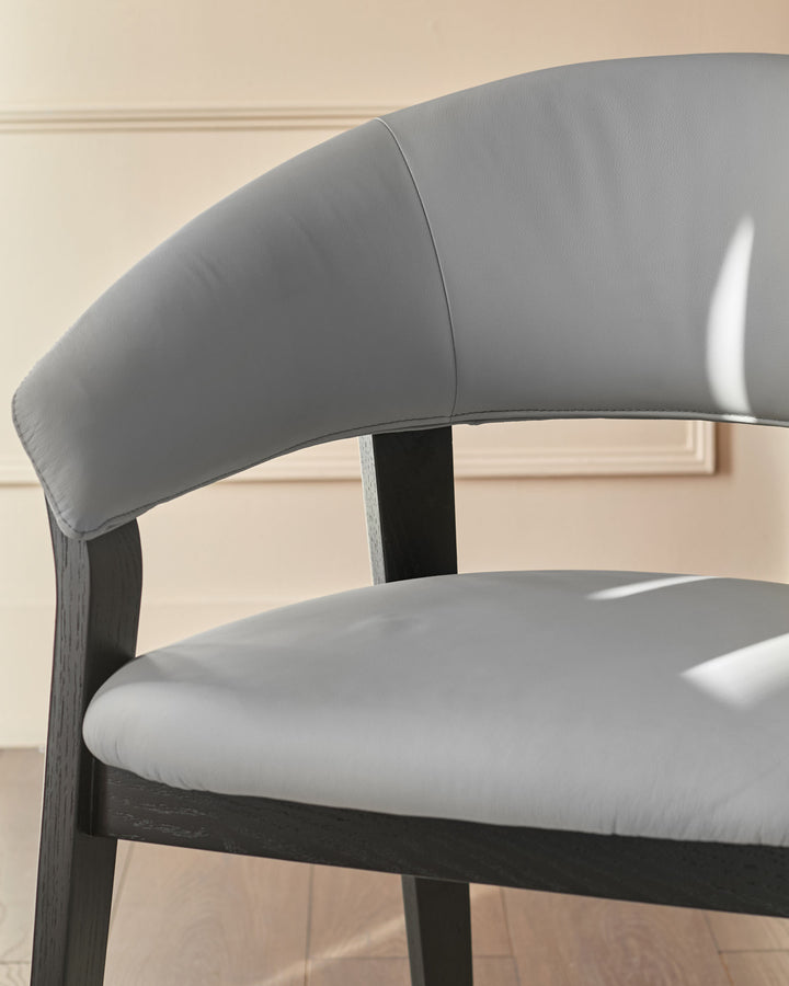 Amelia dining chair in light grey leather with dark wood frame, shown from a side angle highlighting the curved backrest.