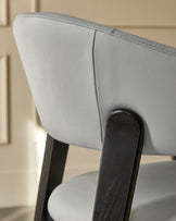 Light grey leather dining chair with black wooden legs, shown from a close-up side angle highlighting the curved backrest.