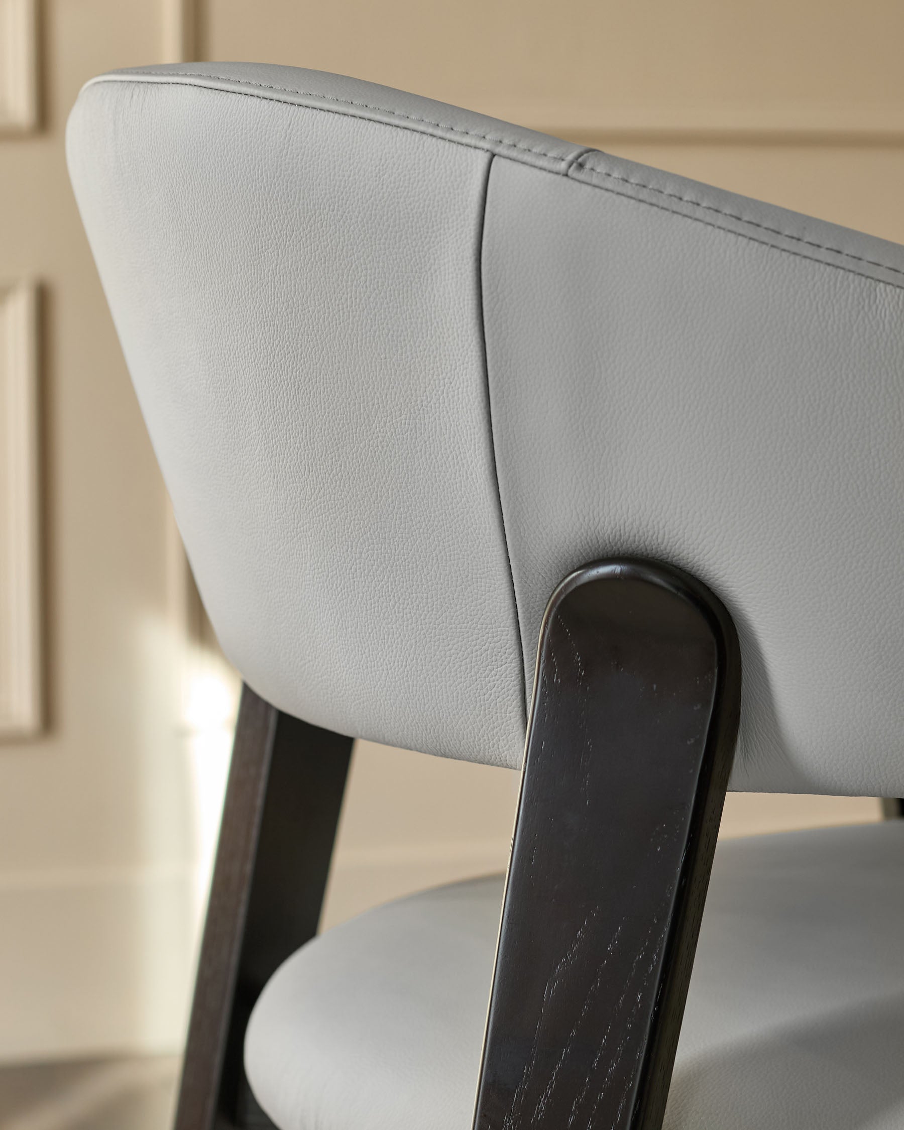 Light grey leather dining chair with black wooden legs, shown from a close-up side angle highlighting the curved backrest.