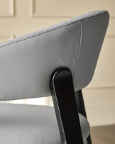 Light grey leather dining chair detail showing curved backrest and black wooden leg support.