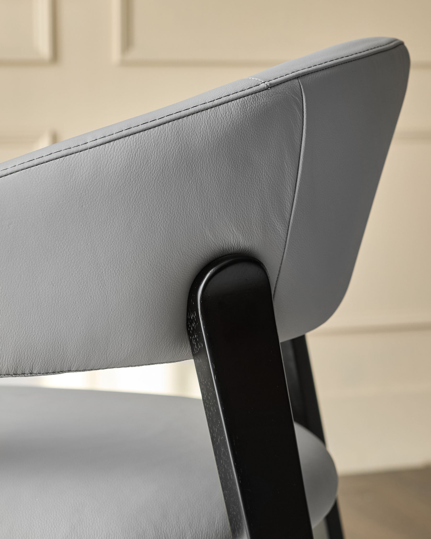 Light grey leather dining chair detail showing curved backrest and black wooden leg support.