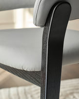 Amelia dining chair close-up showing light grey leather seat and black wood frame detail.