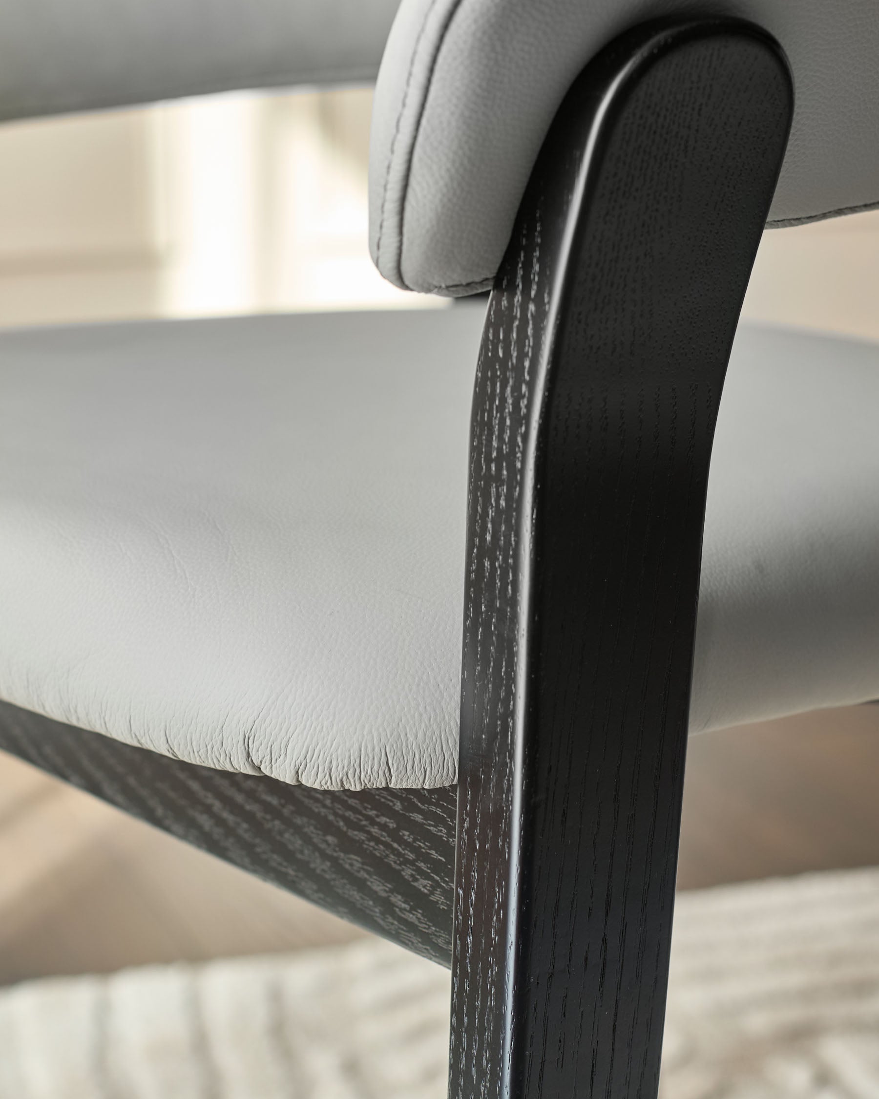 Amelia dining chair close-up showing light grey leather seat and black wood frame detail.