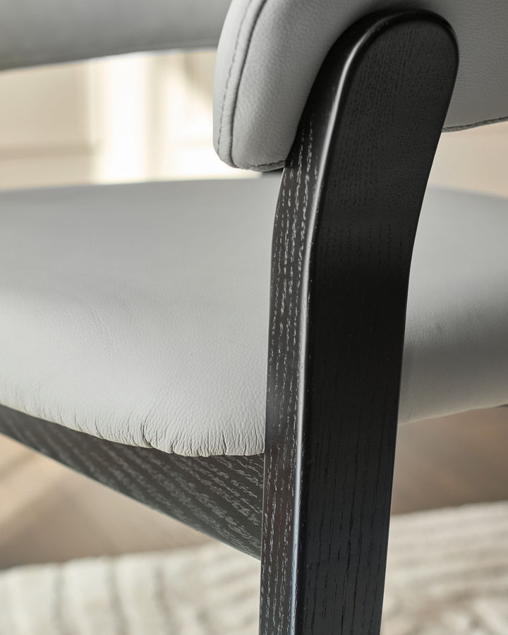 Amelia dining chair close-up showing light grey leather seat and black wood frame detail.