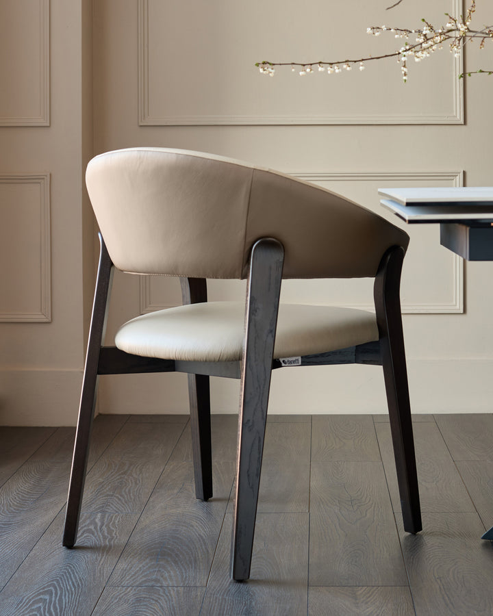 Amelia dining chair in natural leather and mocha wood, shown from a three-quarter view in an elegant interior setting.