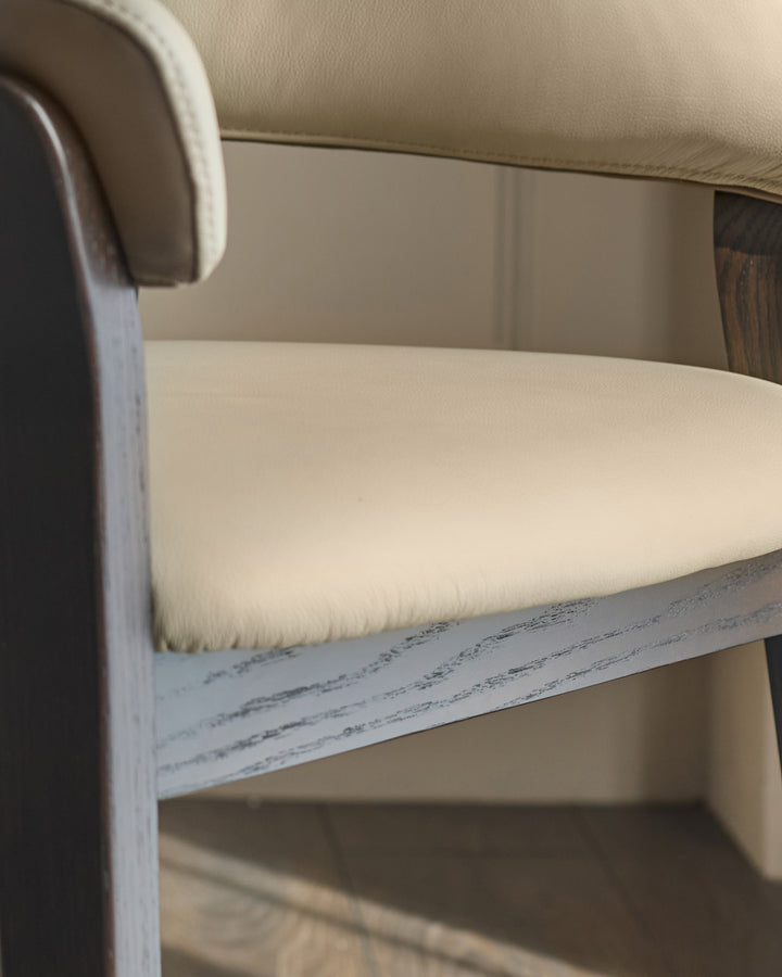Amelia Dining Chair detail showing natural leather seat, mocha wooden frame, and curved armrest from side angle.