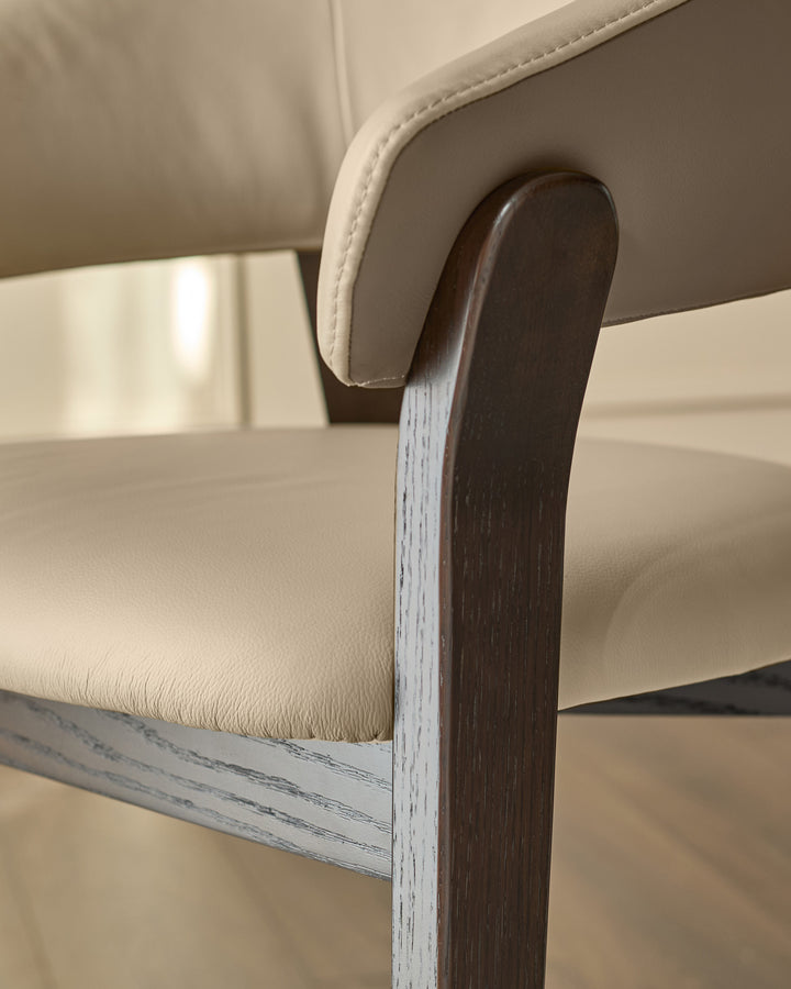 Amelia dining chair detail showing cream leather seat and backrest with curved wooden armrest and whitewashed wood frame.