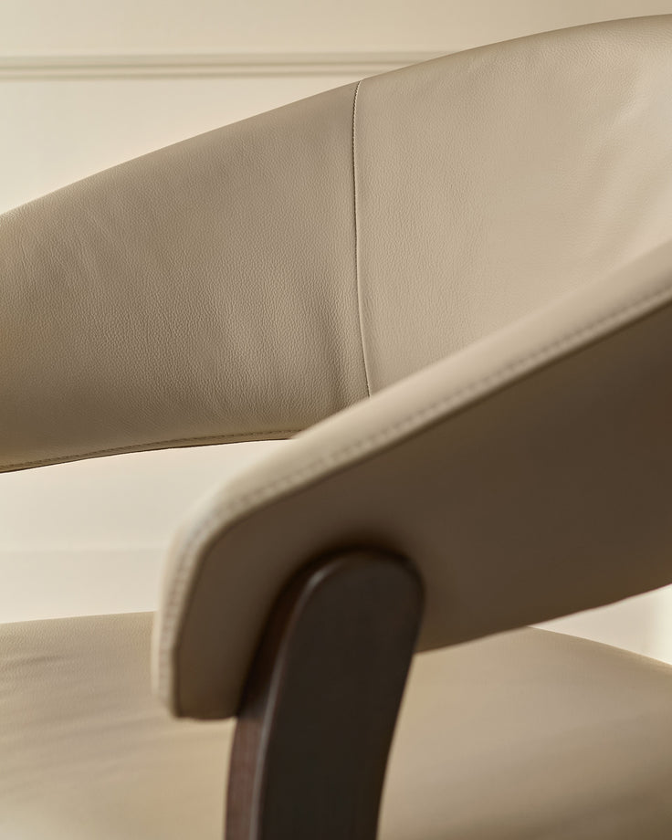 Amelia dining chair in natural leather, close-up of curved backrest and wooden frame detail.