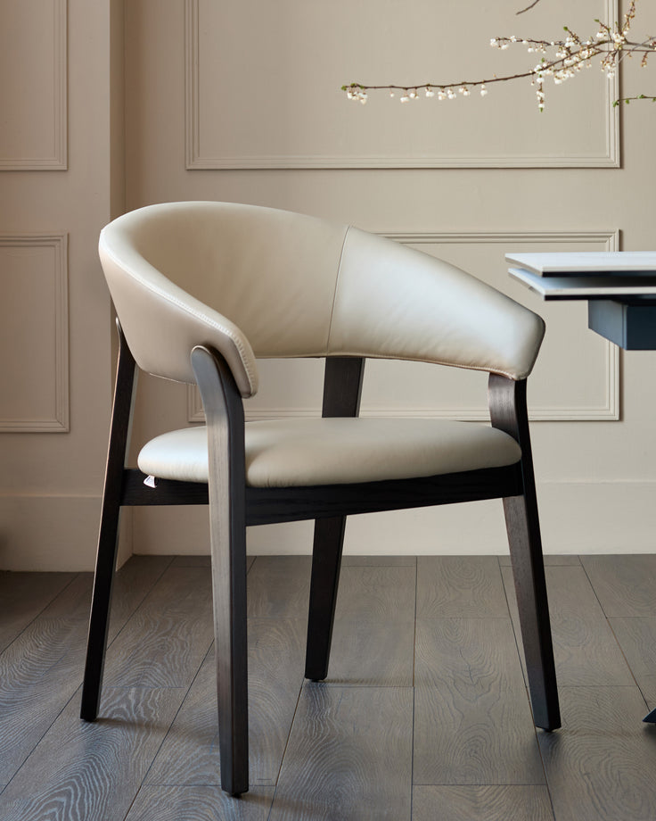 Amelia dining chair in natural leather with mocha wood frame, curved backrest, shown in modern room setting.