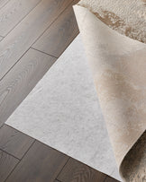 A beige patterned rug with a white underlay, laying on a wood laminate floor. Focus is on the rug and flooring.