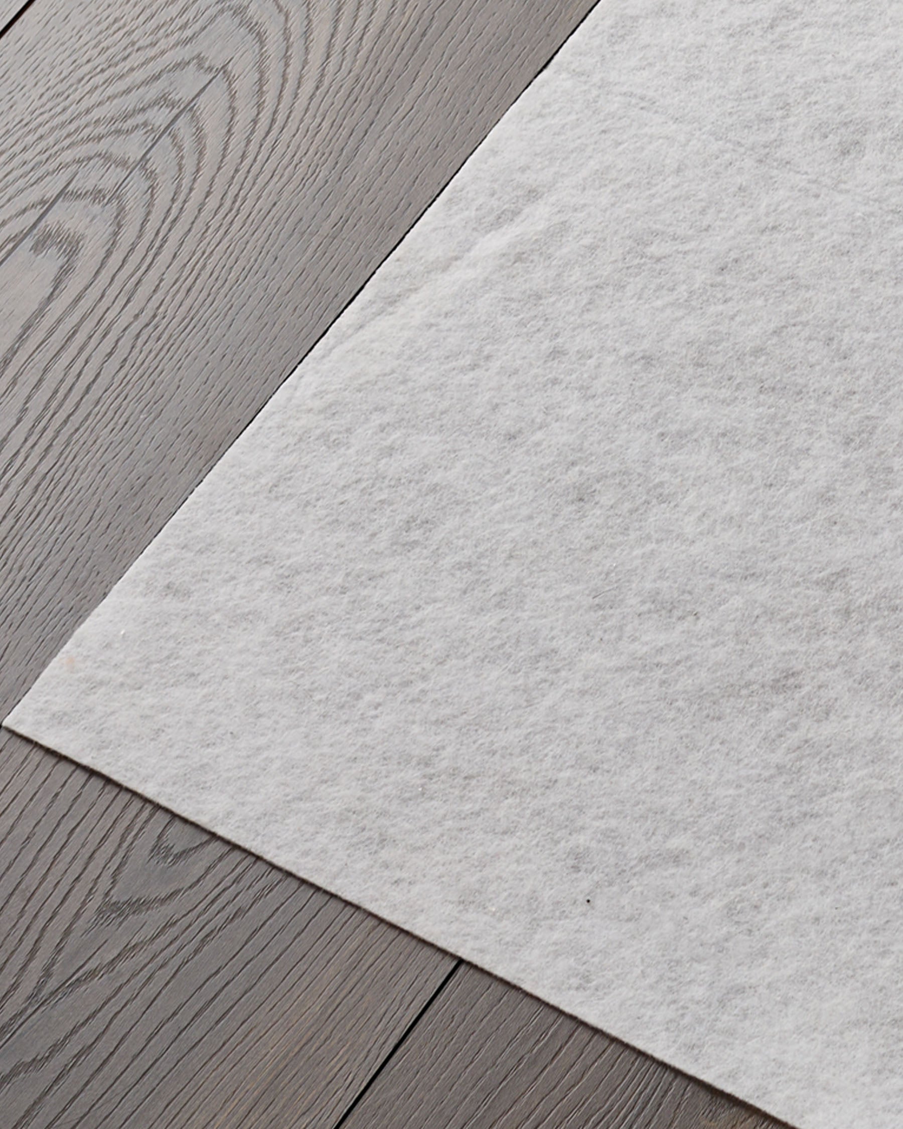 Close-up of grey laminate flooring and a white felt pad. Ideal for underlay or soundproofing, with a modern feel.