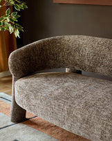 Mocha fabric accent sofa with curved back and cylindrical legs, angled side view on geometric area rug.