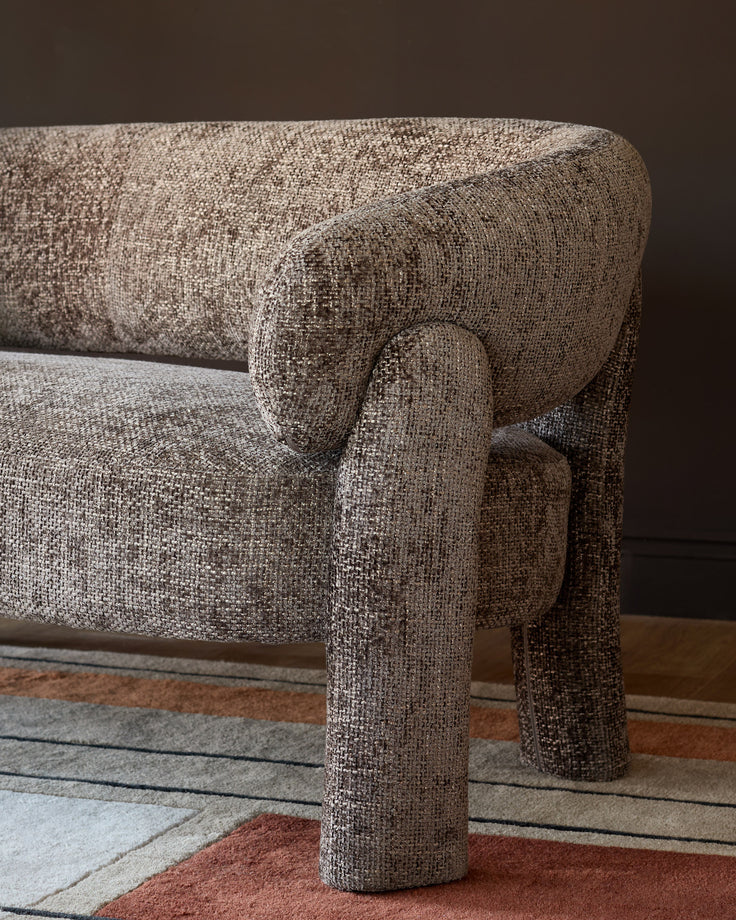 Anya accent sofa in mocha fabric, close-up detail of rolled arm and cylindrical leg on colorful area rug.
