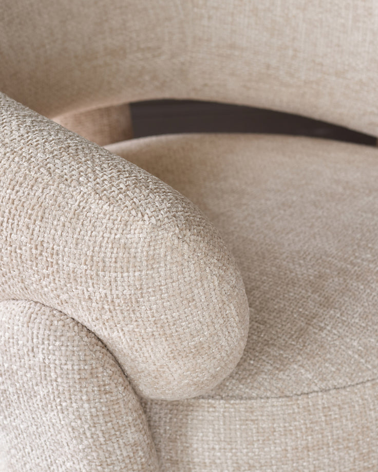 Anya accent chair in natural fabric, close-up of rolled arm and metal frame detail.