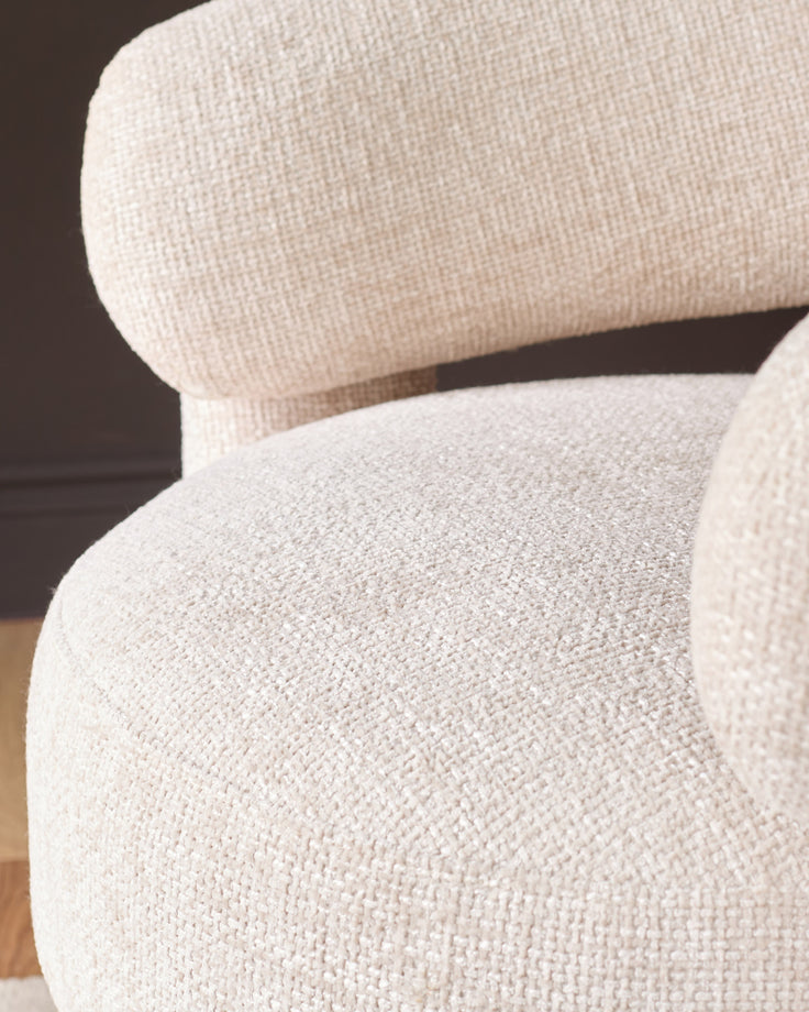 Anya accent chair in natural fabric, close-up detail showing curved armrest and seat upholstery texture.