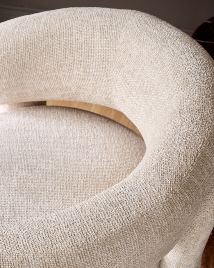 Anya accent chair in natural fabric, close-up of curved backrest and wooden handle detail.