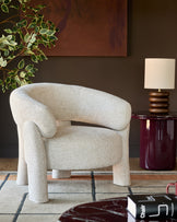 Anya accent chair in natural fabric with curved backrest and chunky cylindrical legs, styled in a modern living room setting.