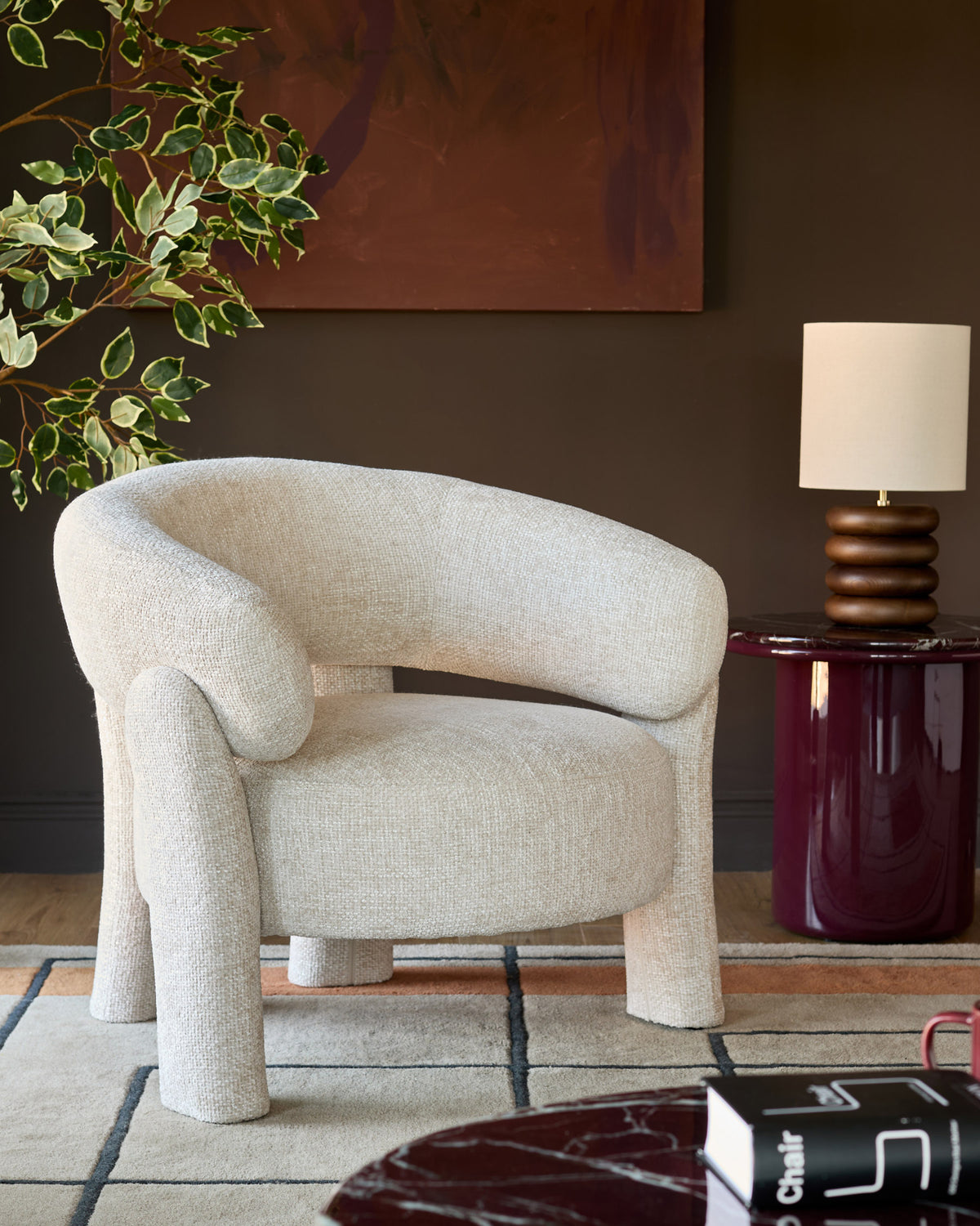 Anya accent chair in natural fabric with curved backrest and chunky cylindrical legs, styled in a modern living room setting.