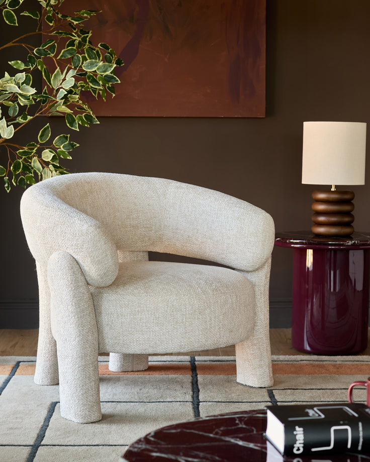 Anya accent chair in natural fabric with curved backrest and chunky cylindrical legs, styled in a modern living room setting.