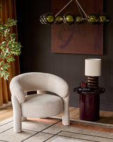 Anya accent chair in natural fabric with curved arms and backrest, shown in a styled room setting with side table and lamp.