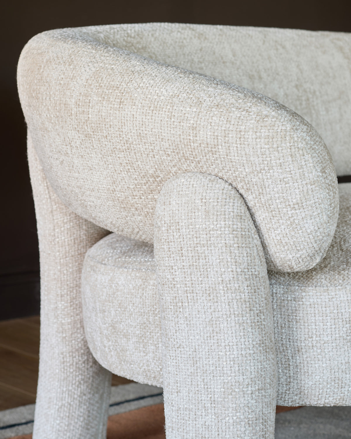 Anya accent sofa in natural fabric, close-up side view showing curved armrest and textured weave detail.