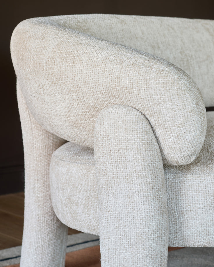 Anya accent sofa in natural fabric, close-up side view showing curved armrest and textured weave detail.