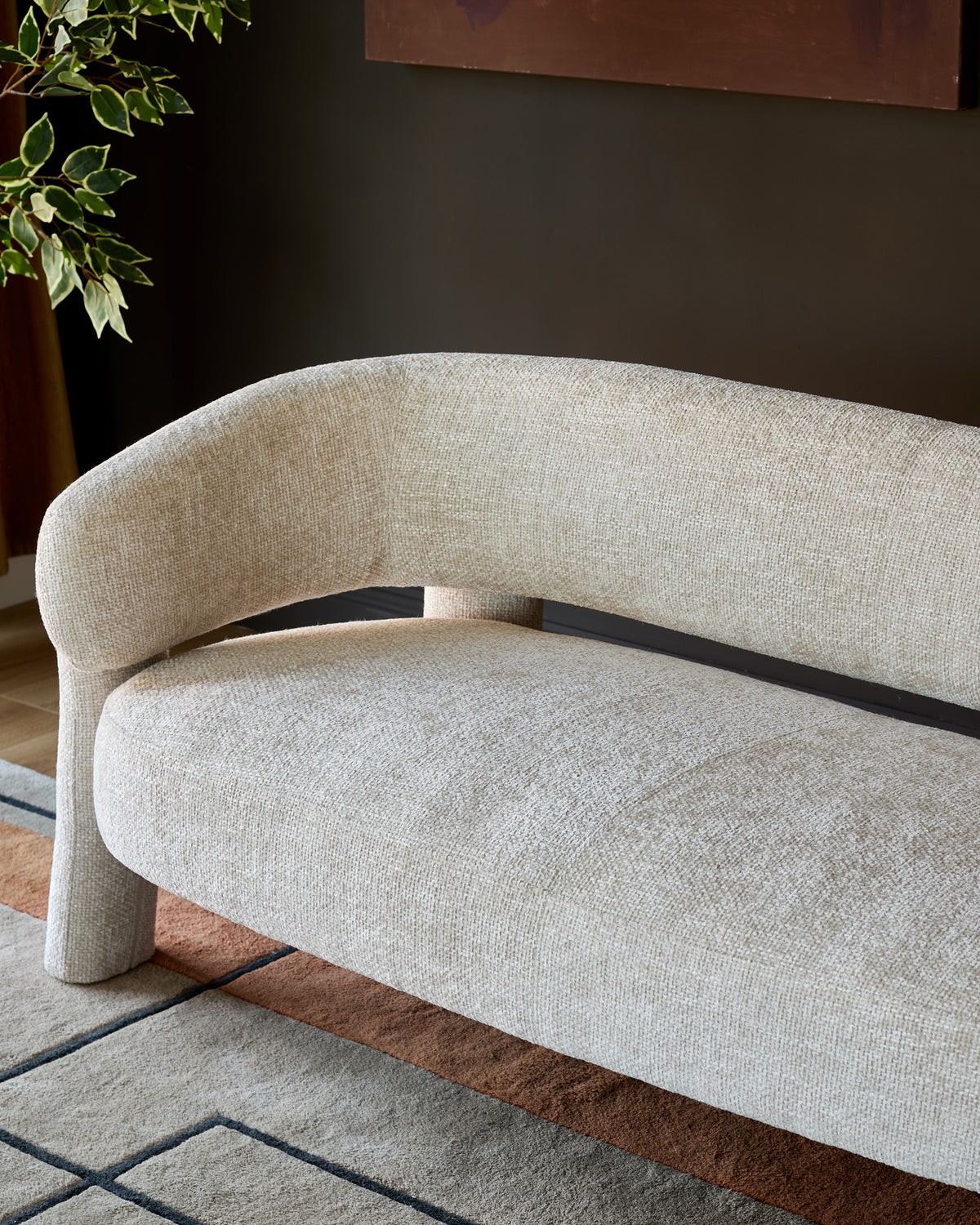 Anya accent sofa in natural fabric, curved design with black wood frame detail, angled view showcasing rounded silhouette.