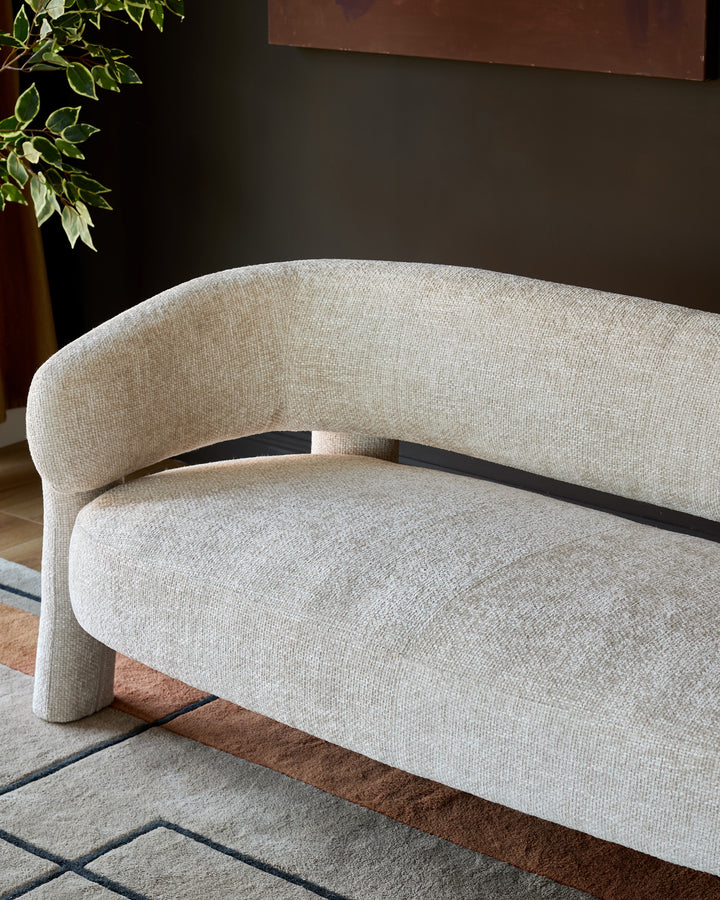 Anya accent sofa in natural fabric, curved design with black wood frame detail, angled view showcasing rounded silhouette.