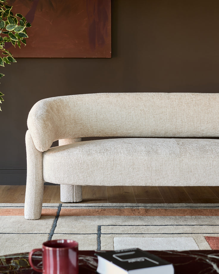 Anya accent sofa in natural fabric, curved design with rounded arms and legs, positioned in modern interior setting.