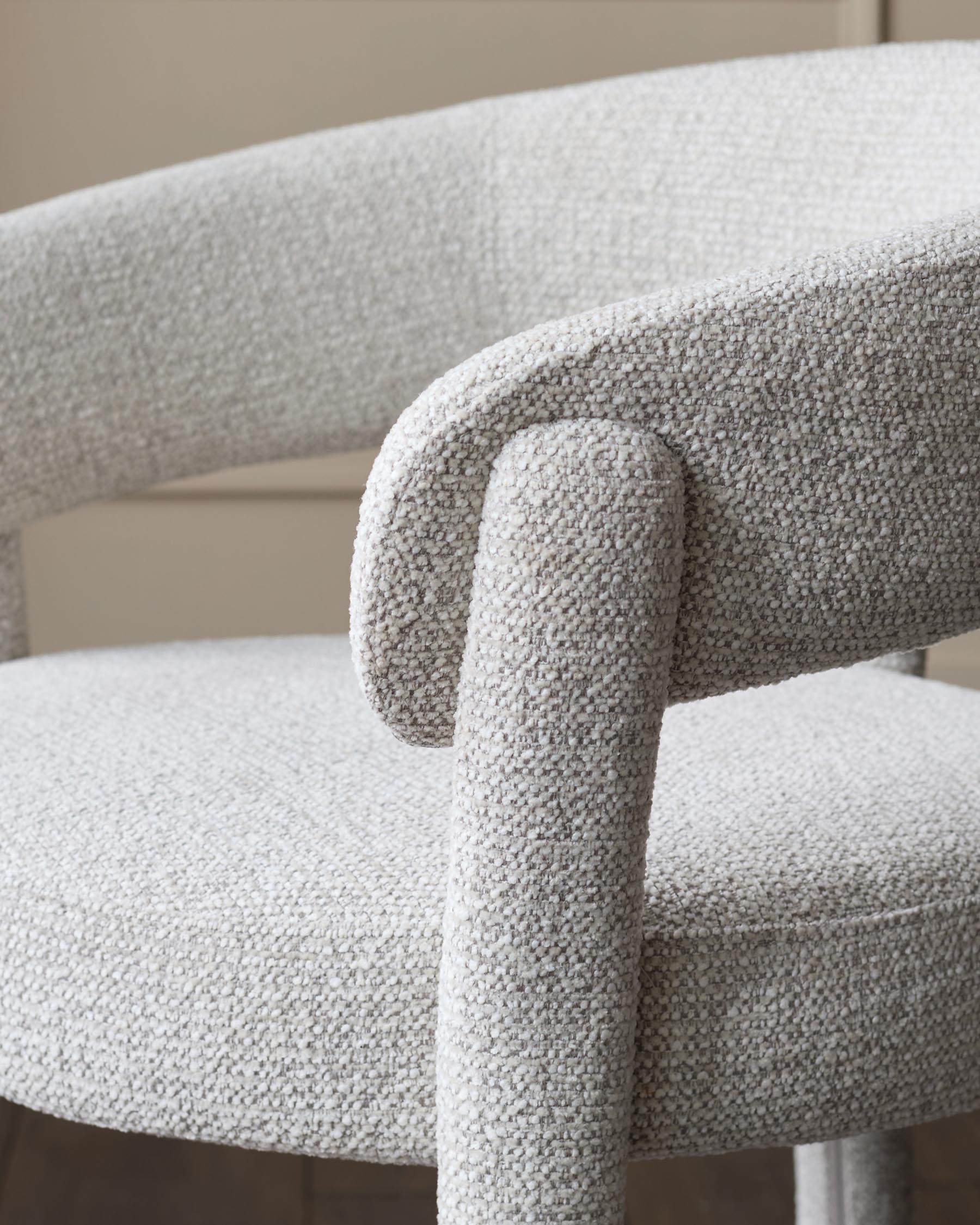 Close-up of a stylish chair with a textured light grey fabric and curved armrest.