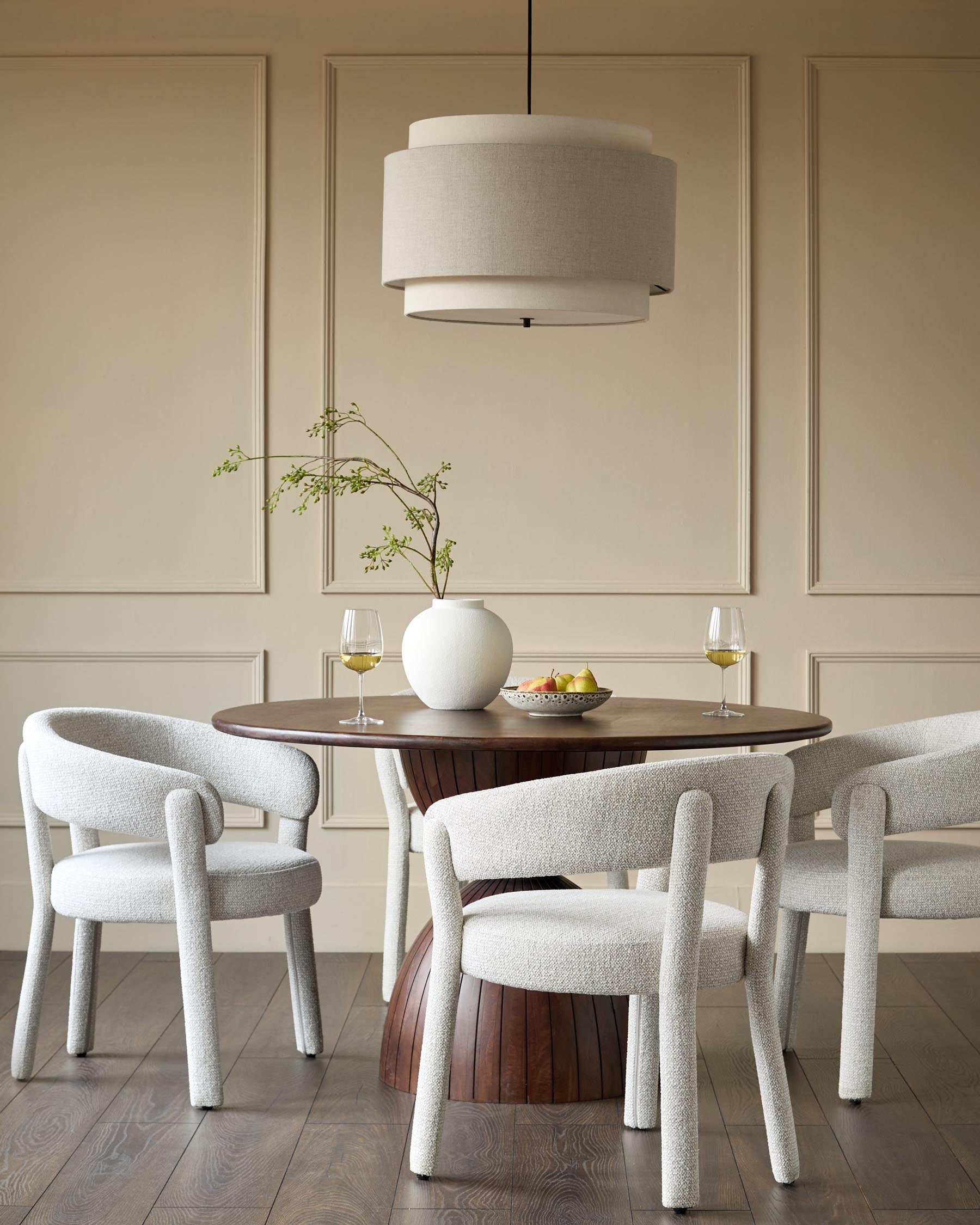 A dining room scene with a round table, upholstered chairs and a statement pendant light.
