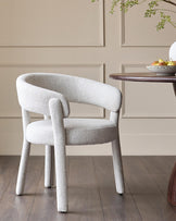 A modern, curved armchair with light grey textured upholstery, alongside a round wood table. Interior design.