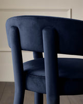 Close-up of a stylish blue velvet chair with a rounded back, showing the texture and design details.