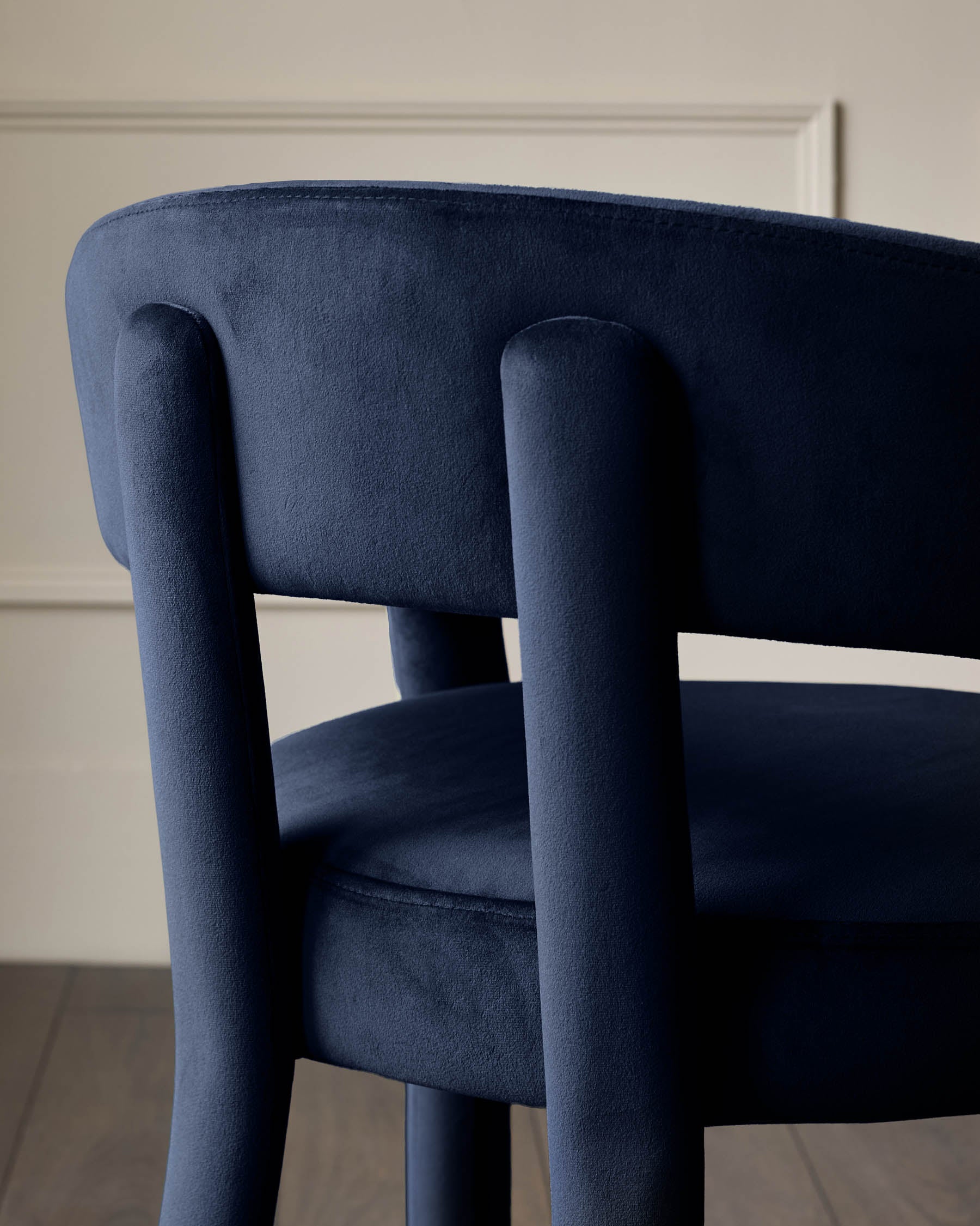 Close-up of a stylish blue velvet chair with a rounded back, showing the texture and design details.