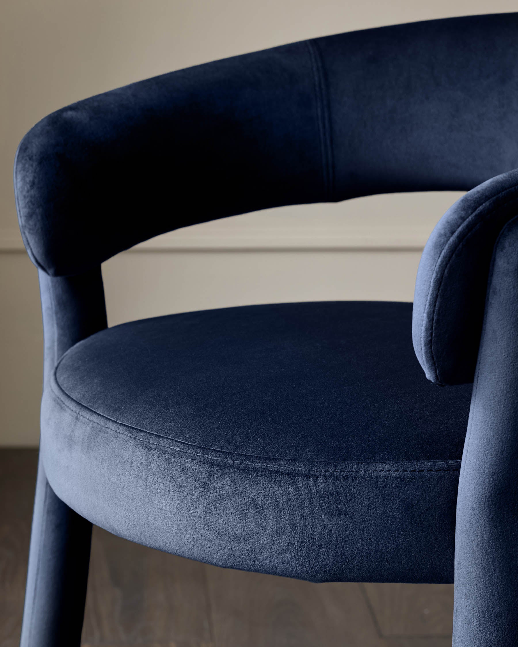 Close up of a navy velvet chair with curved back and seat, showcasing its texture and design.