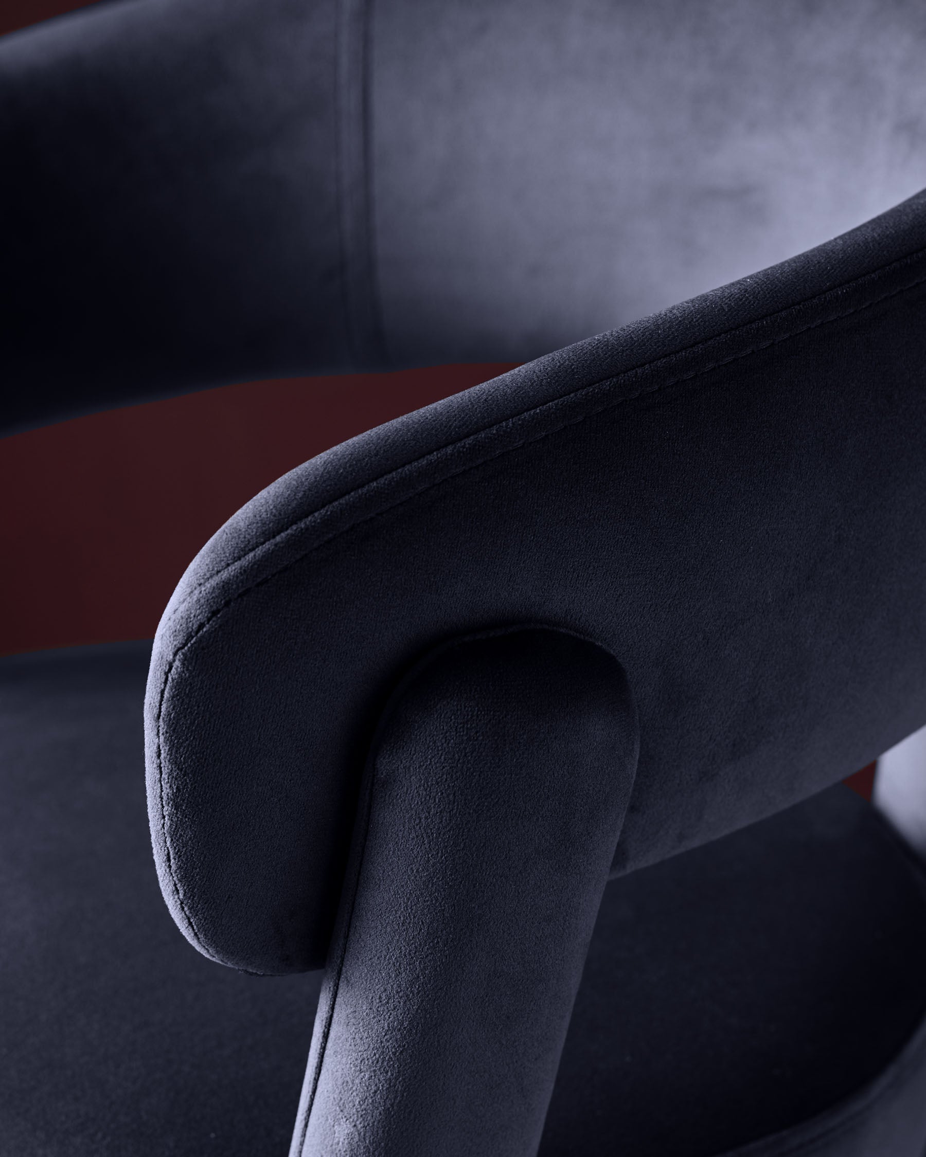Dark navy velvet bar stool with curved armrest, close-up detail shot showing soft upholstery texture and rolled arm design.