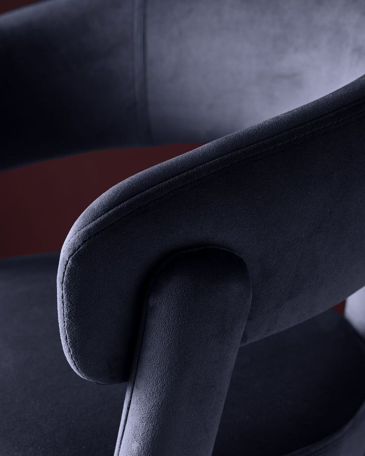 Dark navy velvet bar stool with curved armrest, close-up detail shot showing soft upholstery texture and rolled arm design.