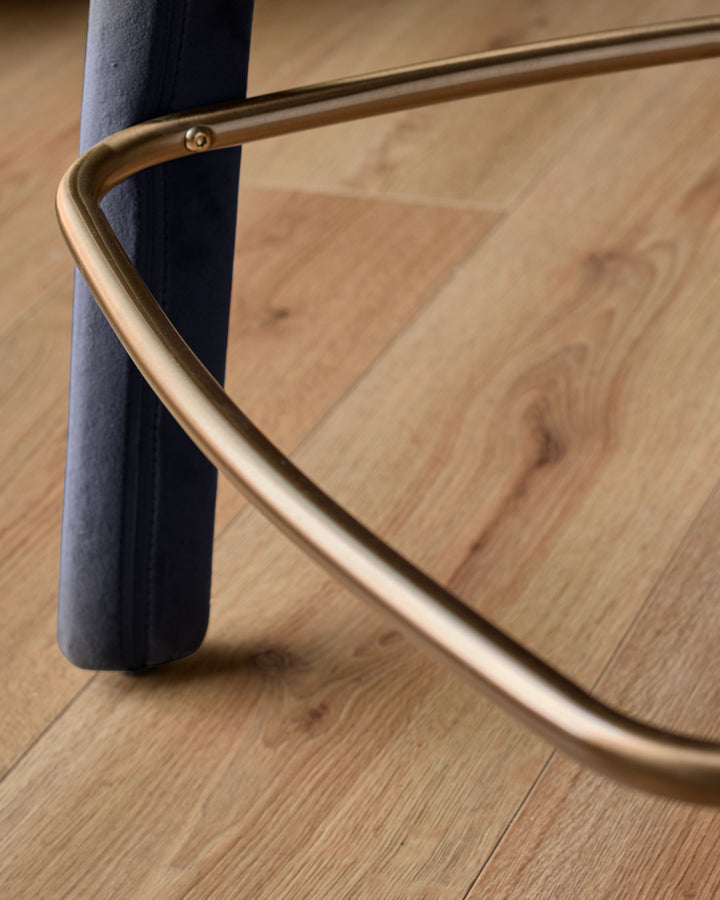 Anya bar stool velvet dark navy - close-up of curved brass handle and leg against wooden floor.