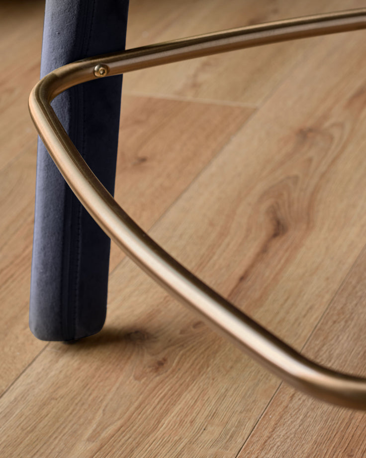 Anya bar stool velvet dark navy - close-up of curved brass handle and leg against wooden floor.