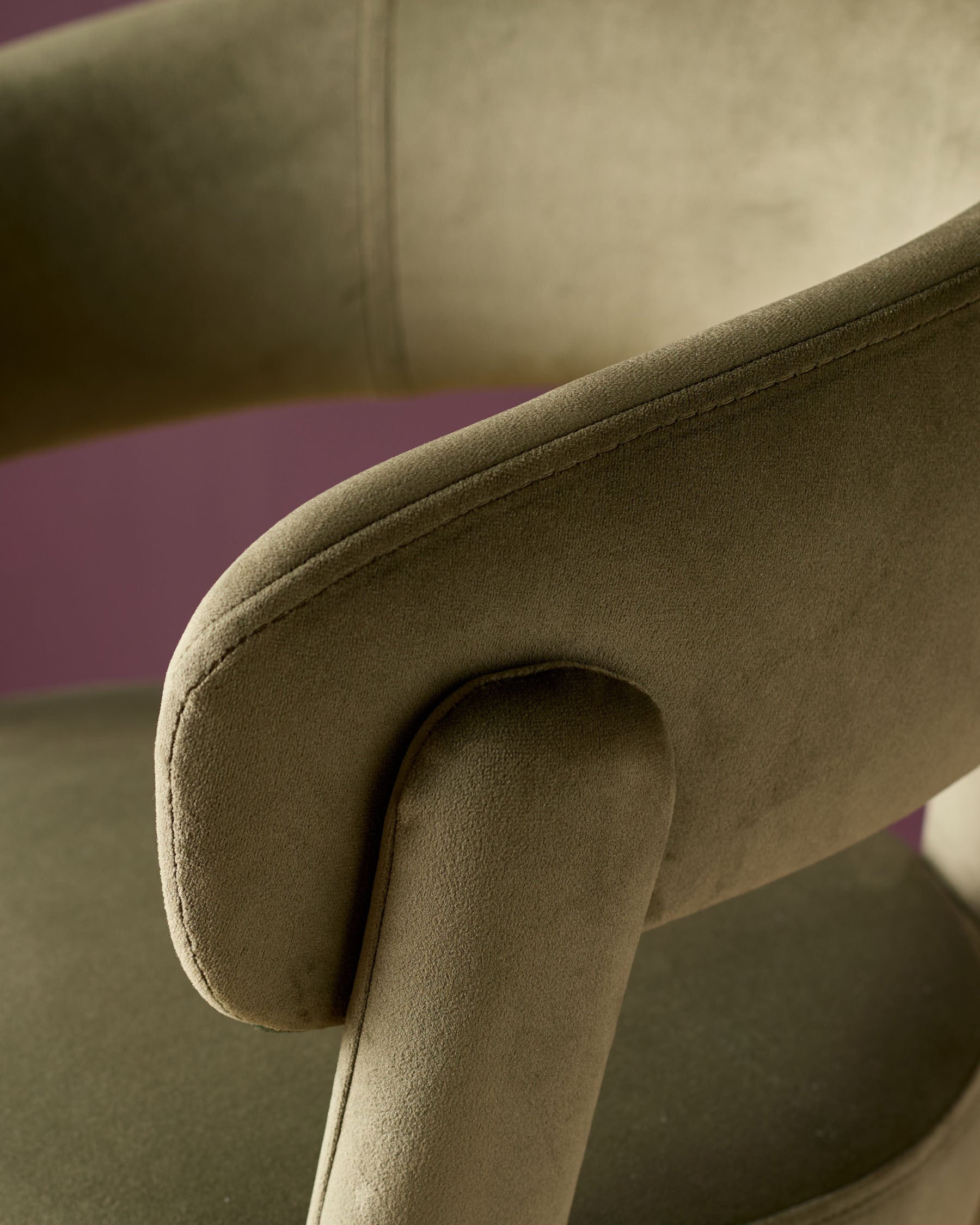 Olive green velvet bar stool with curved armrest and rolled edge detail, close-up side view.