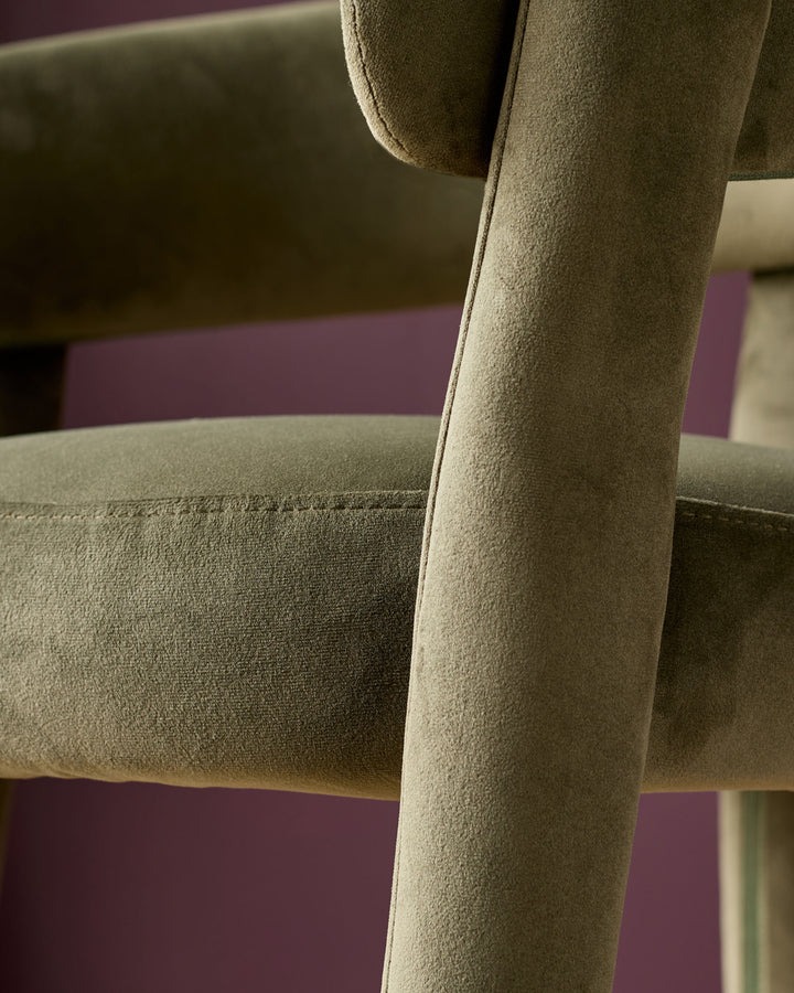 Anya bar stool in olive green velvet, close-up of padded armrest and cylindrical leg detail.
