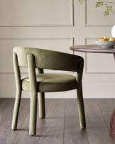 A stylish moss-green velvet chair stands by a wooden table, creating a cosy and inviting dining space.