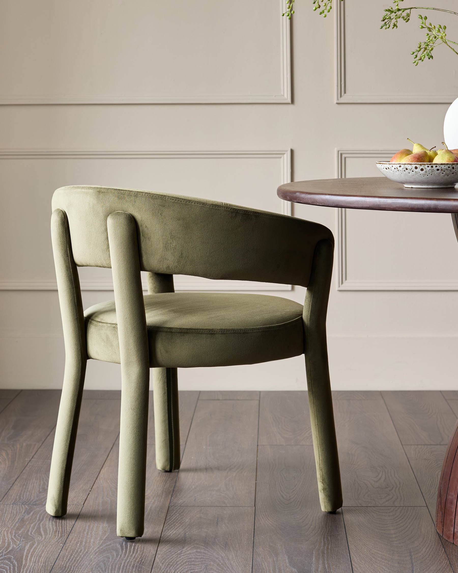 A stylish moss-green velvet chair stands by a wooden table, creating a cosy and inviting dining space.