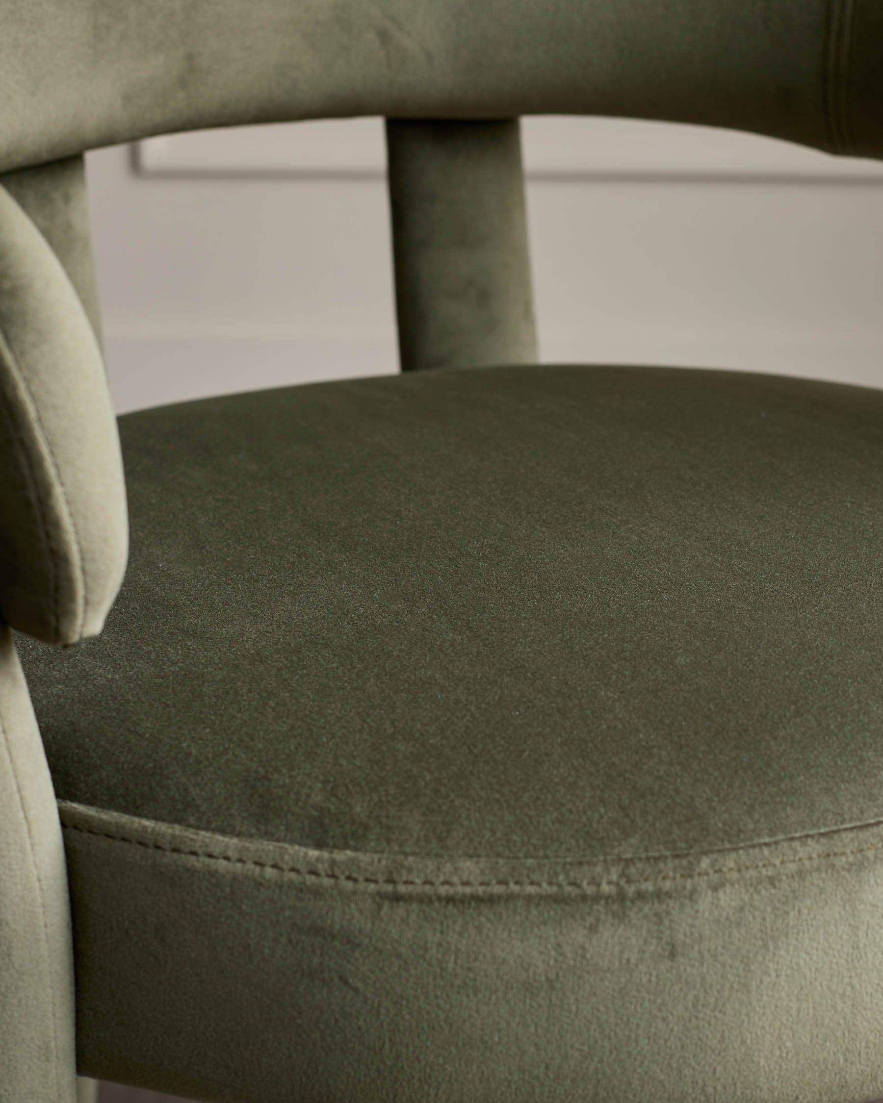 Close-up of an olive green velvet chair, highlighting the texture and detailing of the seat and backrest.