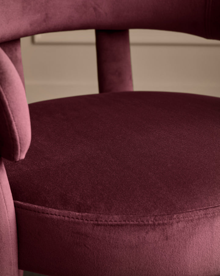 Anya dining chair in plum velvet, showing curved backrest and seat detail from a close-up side angle.