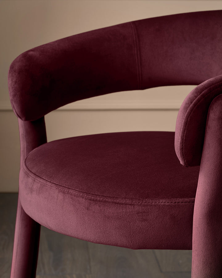 Anya dining chair in plum velvet, shown at an angle highlighting the curved backrest and rounded seat cushion.