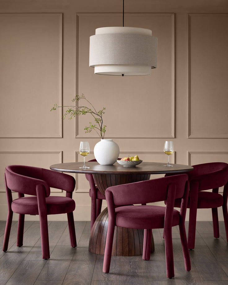 Plum velvet dining chair with curved armrests and cylindrical legs, shown in a styled dining room setting.