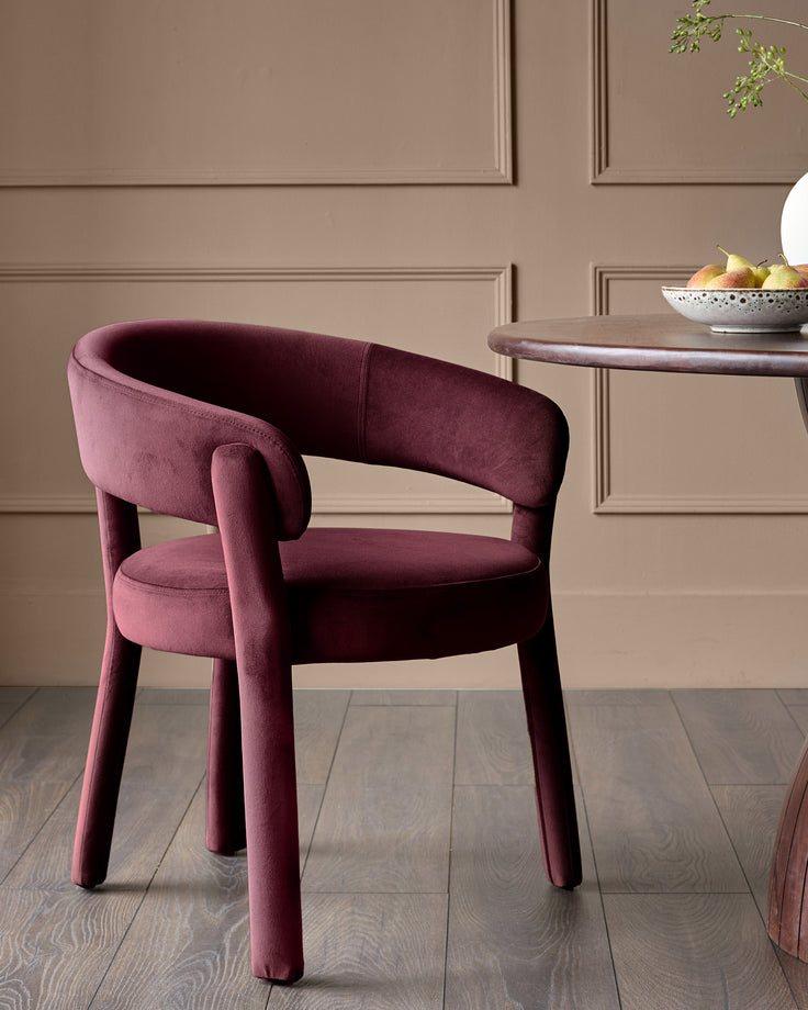 Plum velvet dining chair with curved backrest, rounded armrests, and tapered legs in a modern interior setting.
